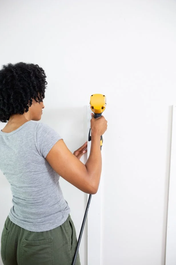 The next step in this DIY accent wall project is to install the vertical trim boards using a pneumatic brad nailer or finish nailer.
